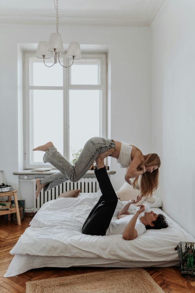 Young couple having fun in bedroom, woman lifted by man on bed.